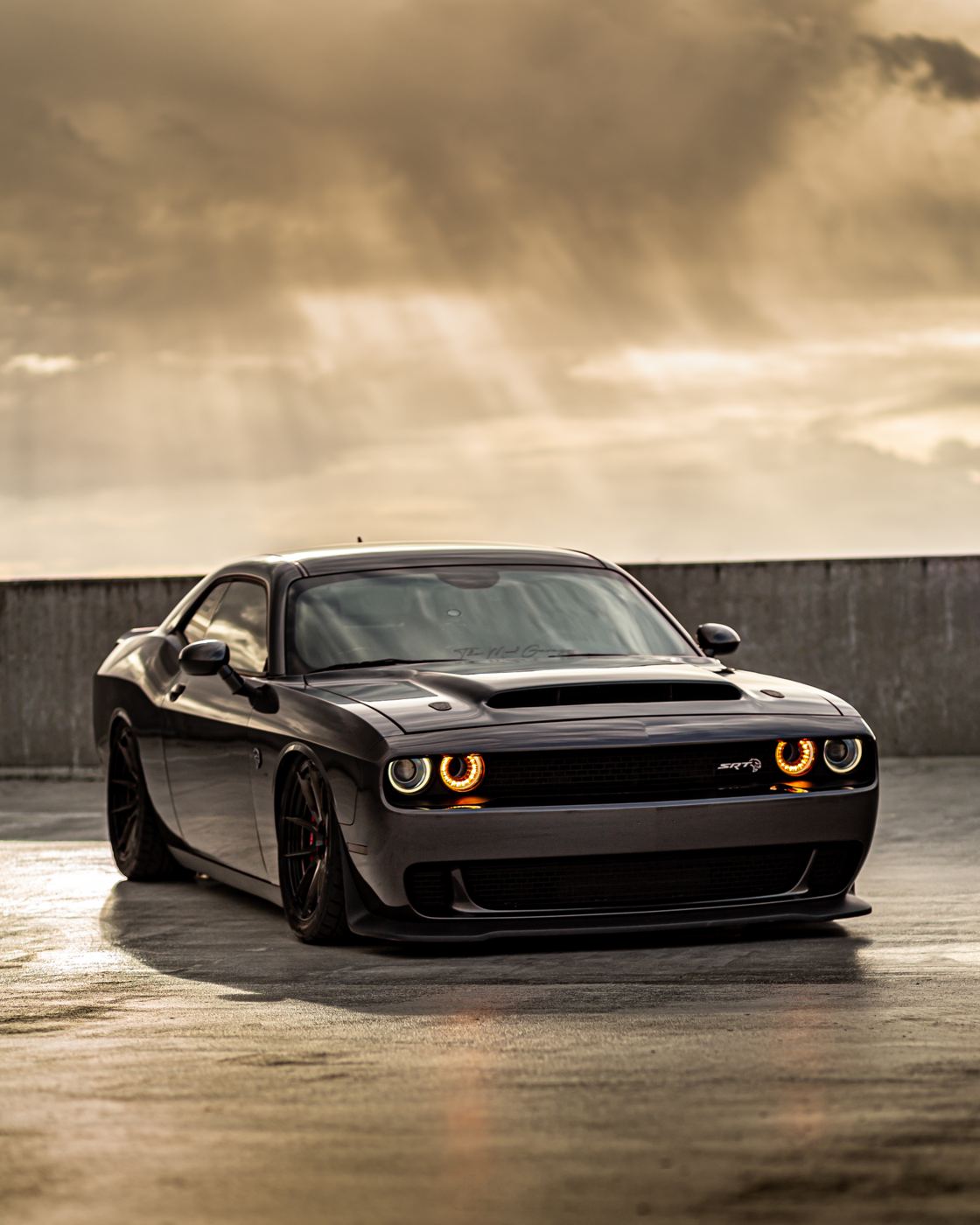 Black Dodge Challenger SRT with halo headlights on a parking deck under a heavy sky
