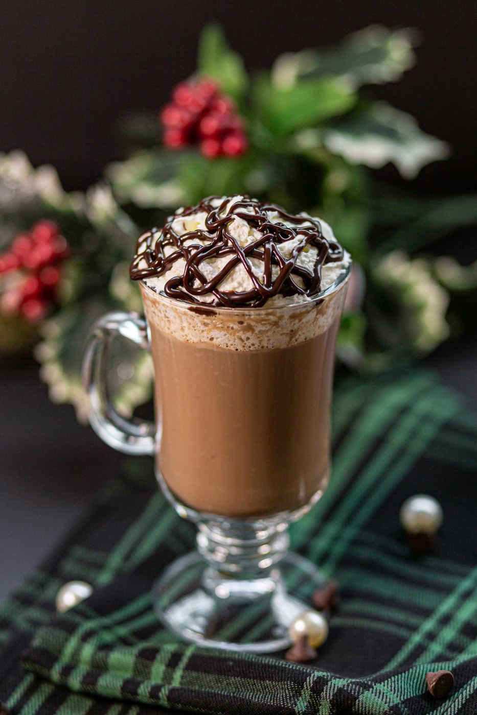 Hot chocolate in a glass mug with whipped cream and holly