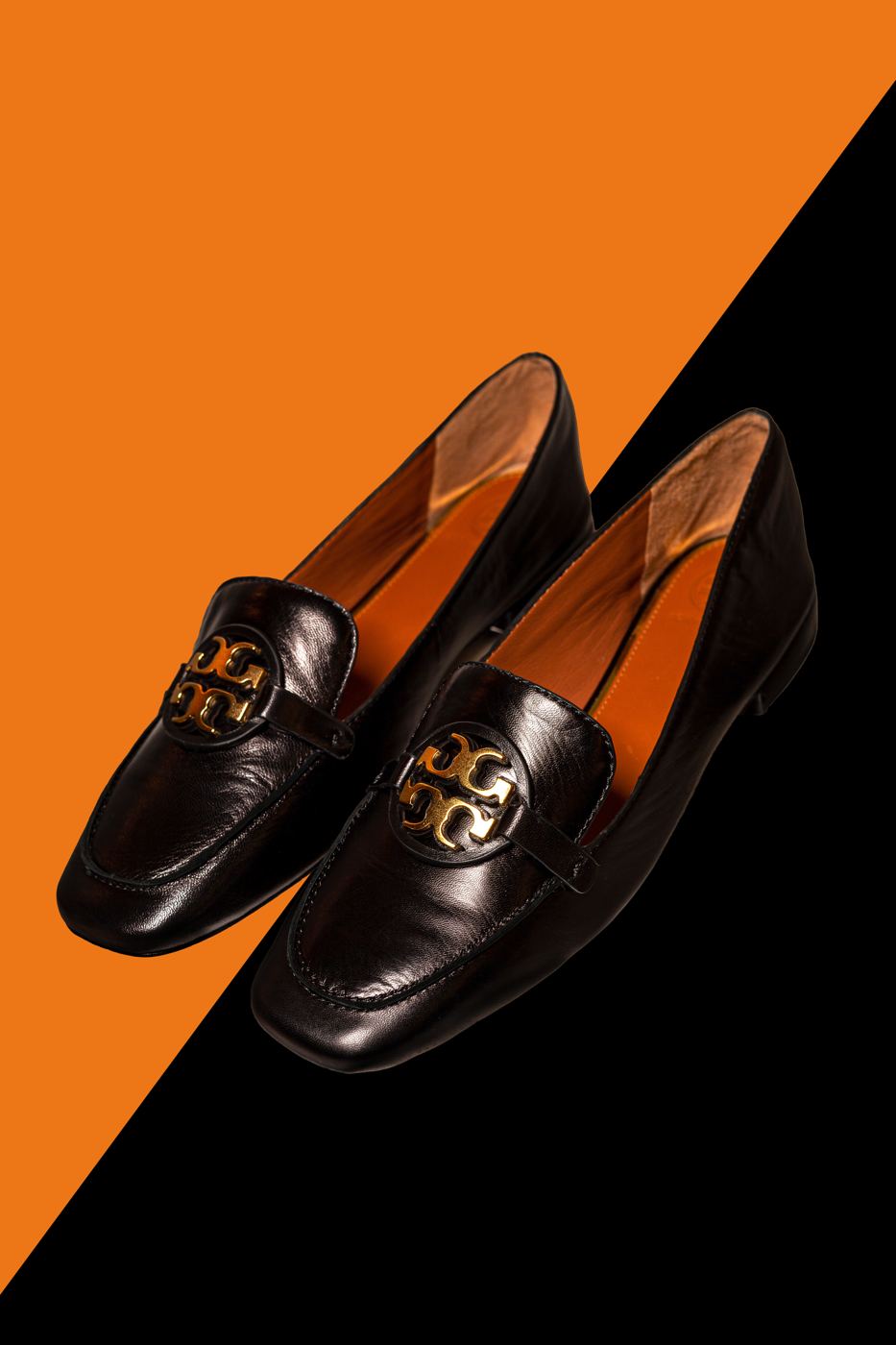 Black leather loafers with gold hardware on an orange and black diagonal set